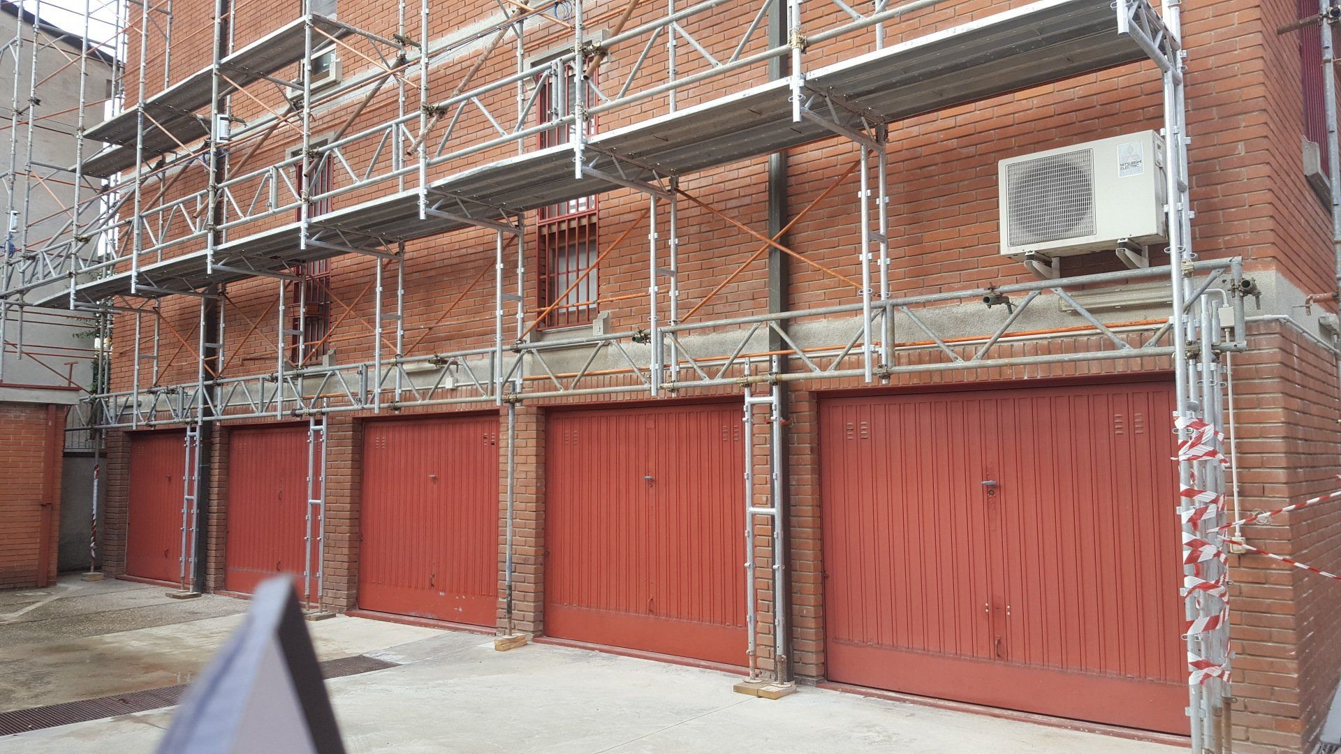 Impalcatura su un edificio in mattoni sopra porte da garage rosse. Condizionatore d'aria montato a parete.