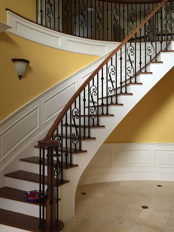 A curved staircase with a wrought iron railing and yellow walls
