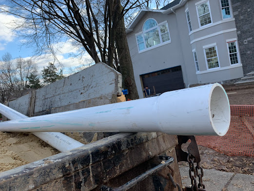 A large white pipe is sitting on top of a truck in front of a house.