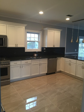 A kitchen with white cabinets , black counter tops , stainless steel appliances and a window.