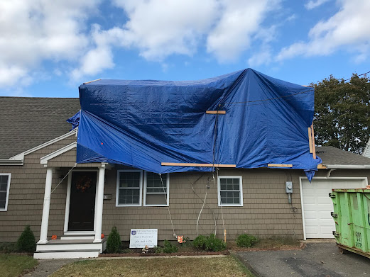 The roof of a house is covered with a blue tarp.