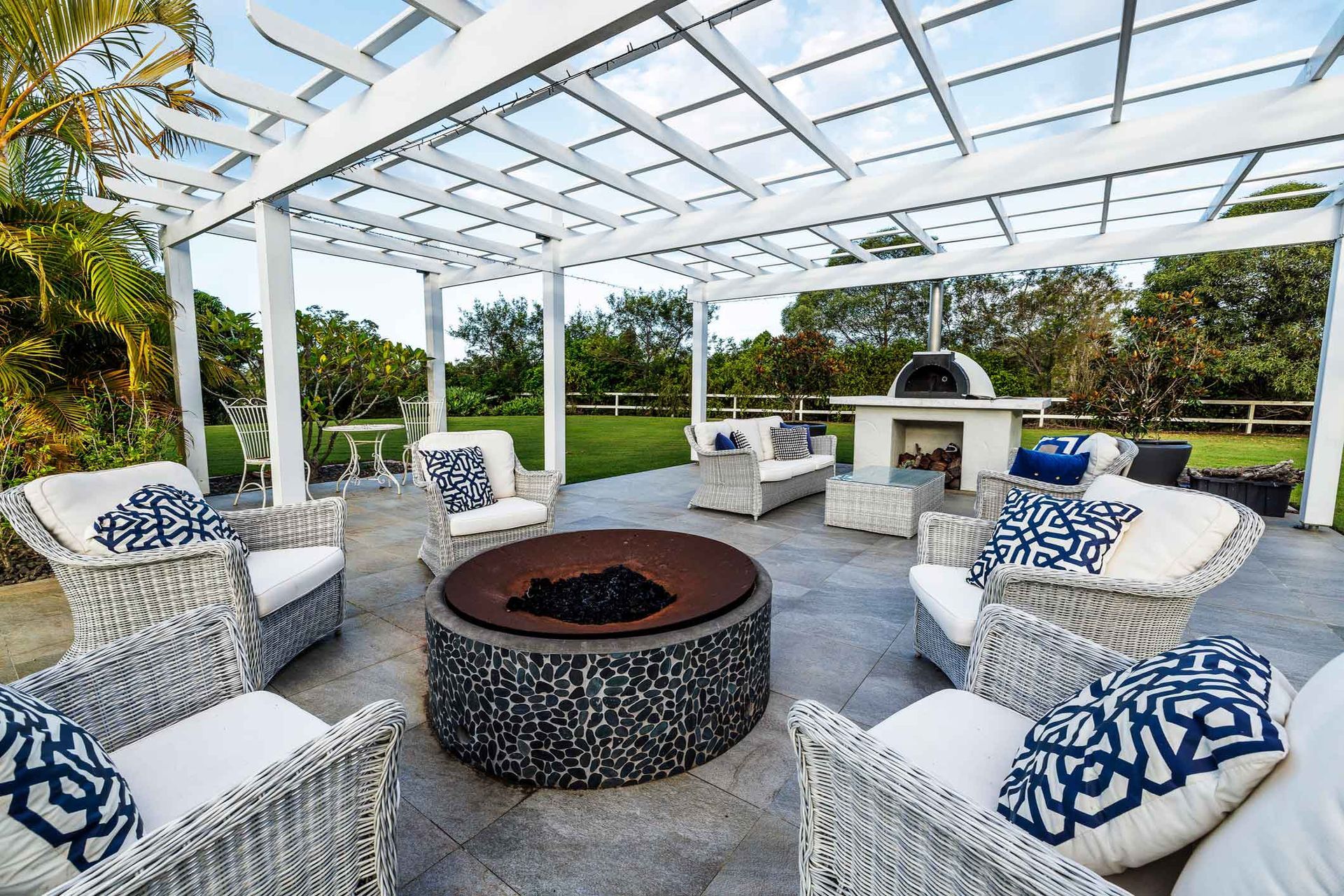A patio with wicker furniture and a fire pit under a pergola