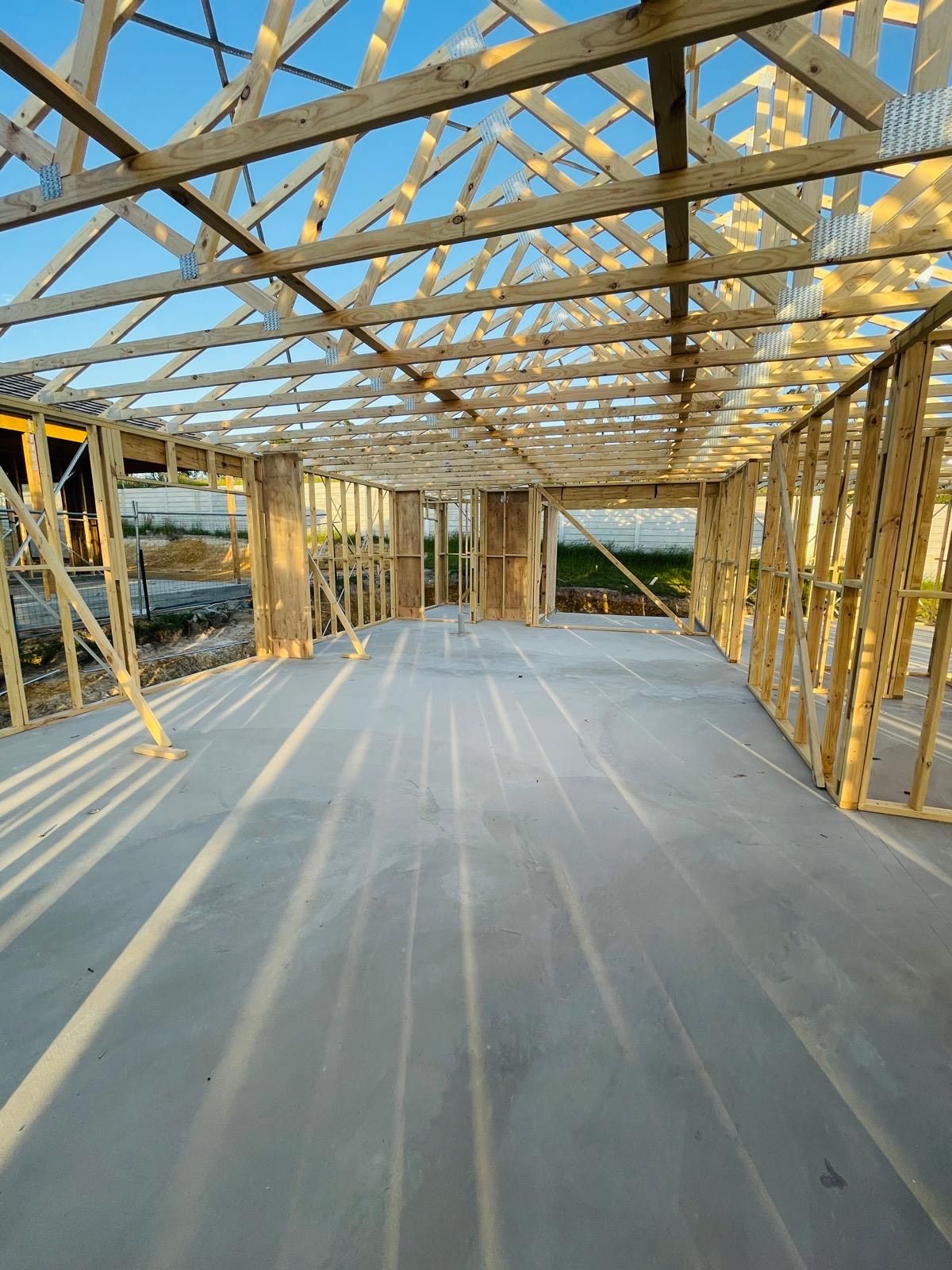 Construction framing of a building interior with concrete floor, wooden beams, and exposed rafters.