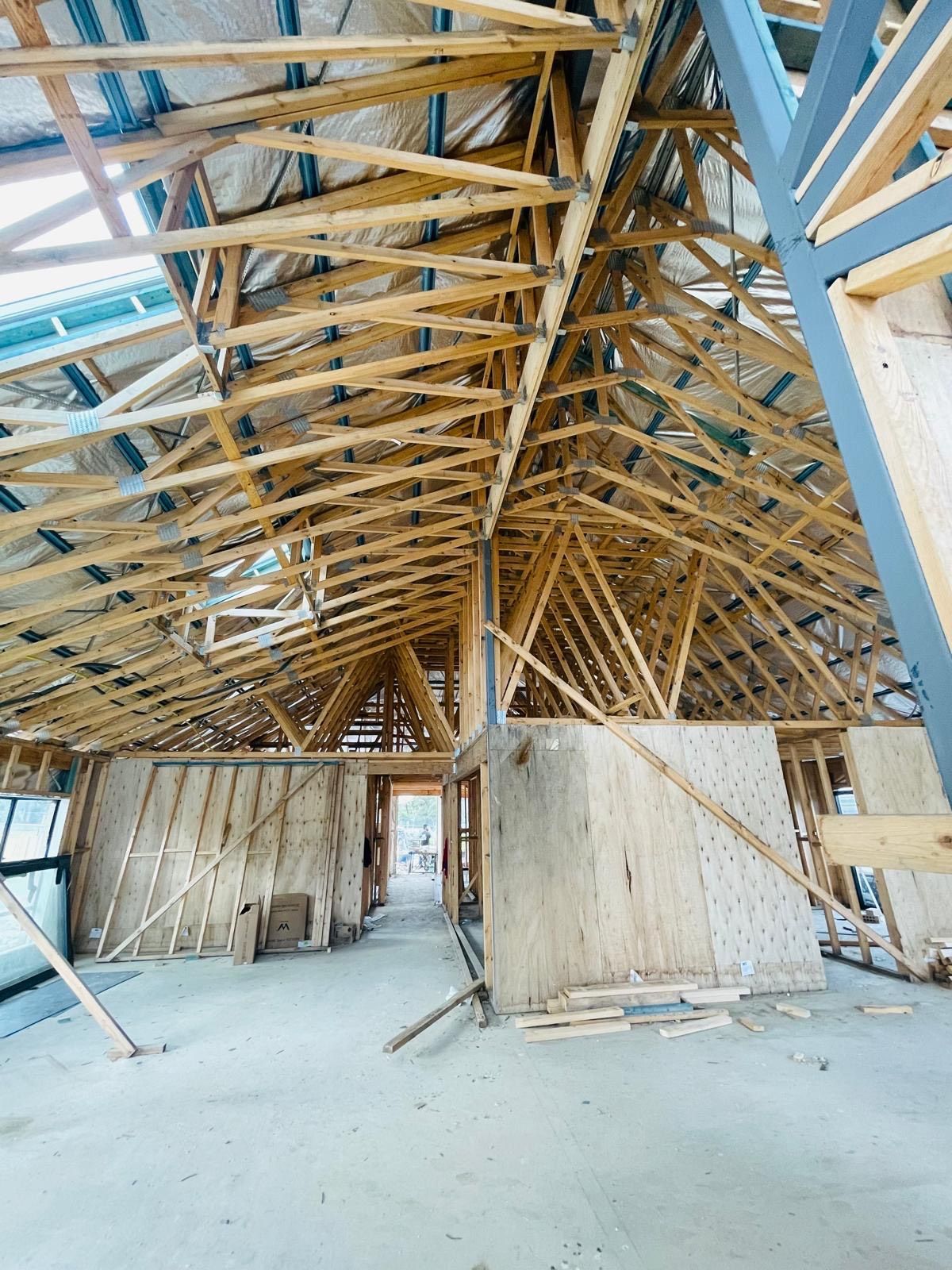 Interior view of a building under construction, showing exposed wooden trusses and framing.