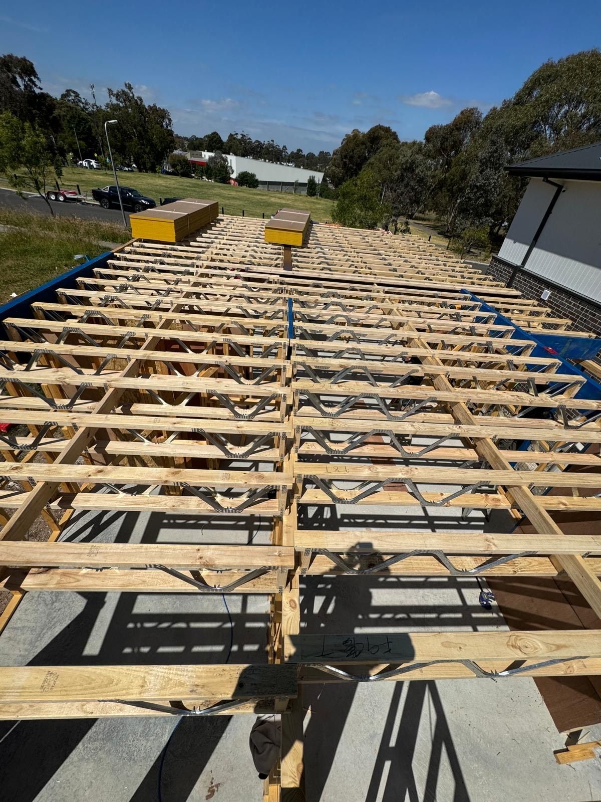Wooden roof trusses under construction, blue tarp, sunny day, clear sky.