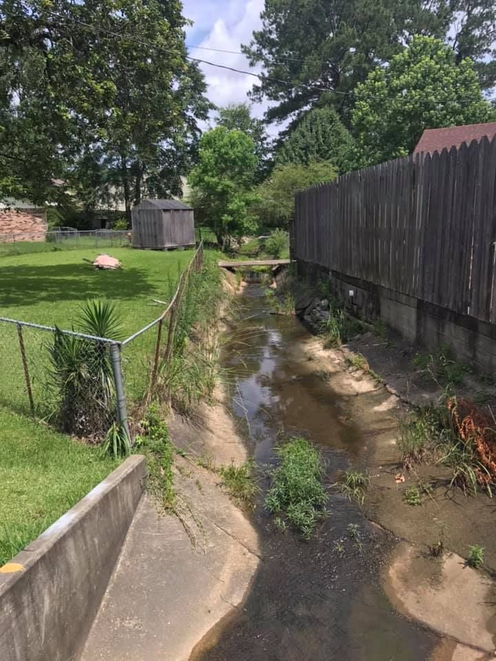 A small stream running through a yard next to a fence.