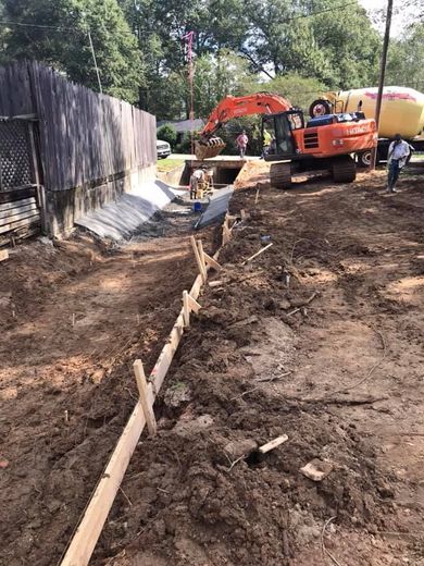 A large excavator is digging a hole in the dirt in front of a fence.