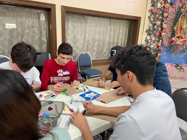 A group of young people are sitting around a table drawing with markers.