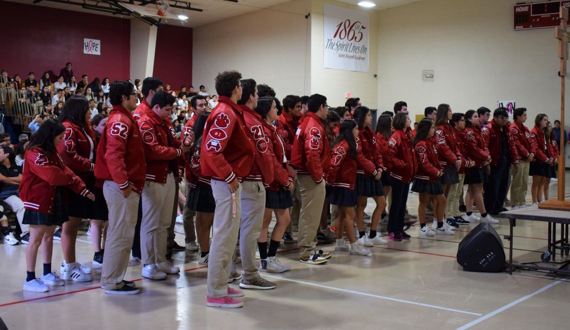 A group of students wearing red jackets stand in a gym
