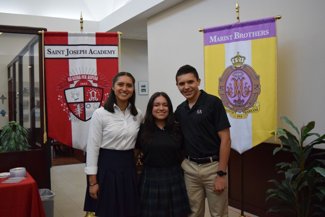 Three people are posing for a picture in front of a banner that says saint joseph academy