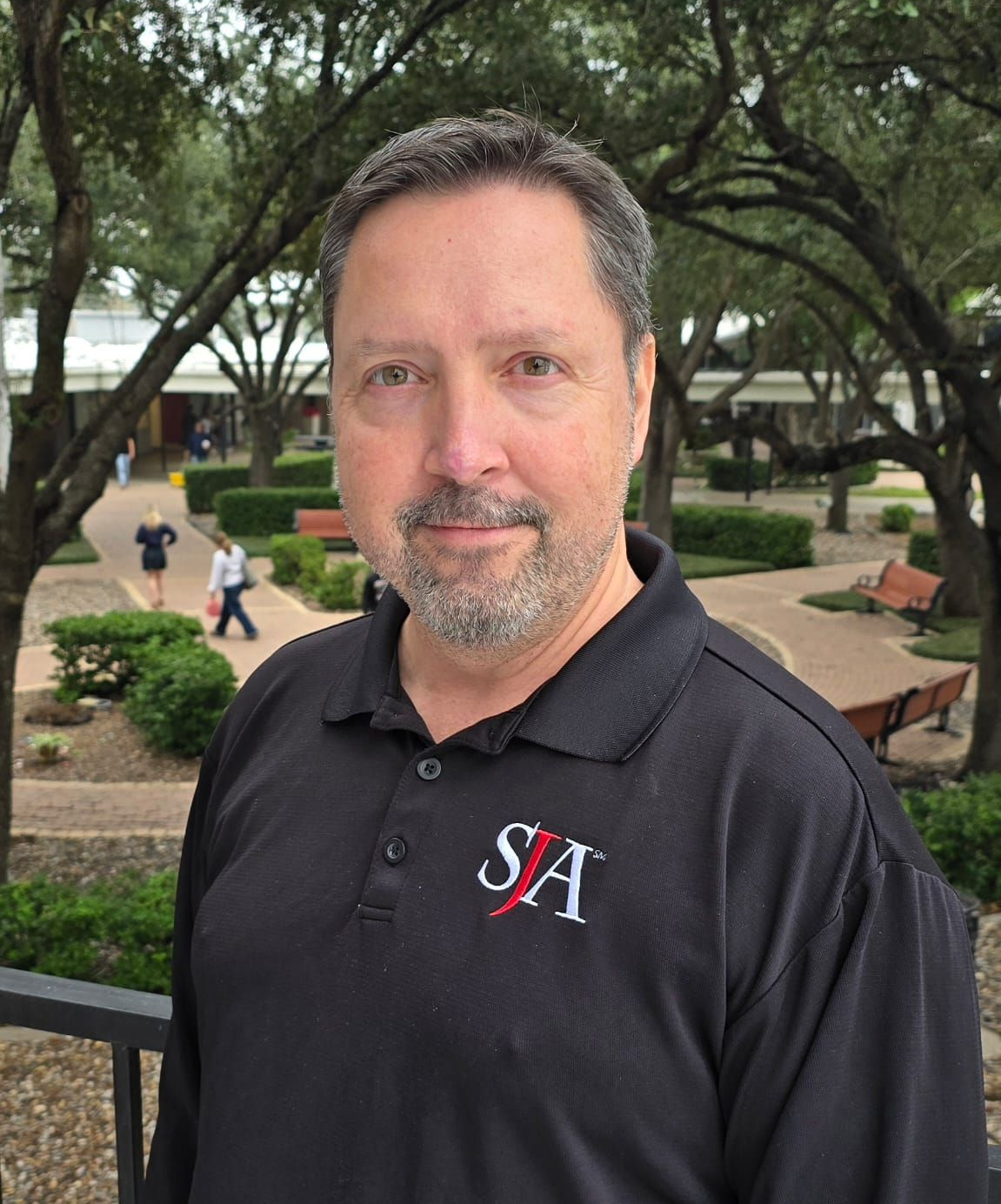 A man in a black jacket is standing in front of a tree
