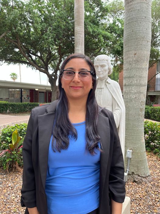 A woman in a blue shirt and black jacket is standing in front of a statue.