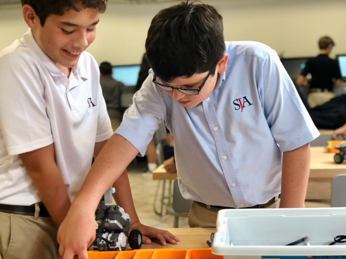 Two boys wearing sa shirts are working on a robot