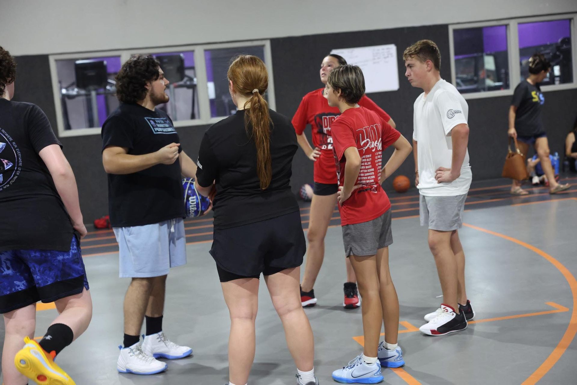 People standing and talking in a gym, with basketball court lines visible.
