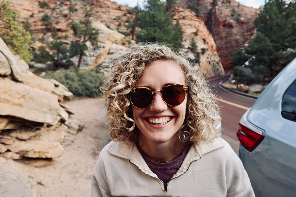 a woman wearing sunglasses is smiling in front of a car