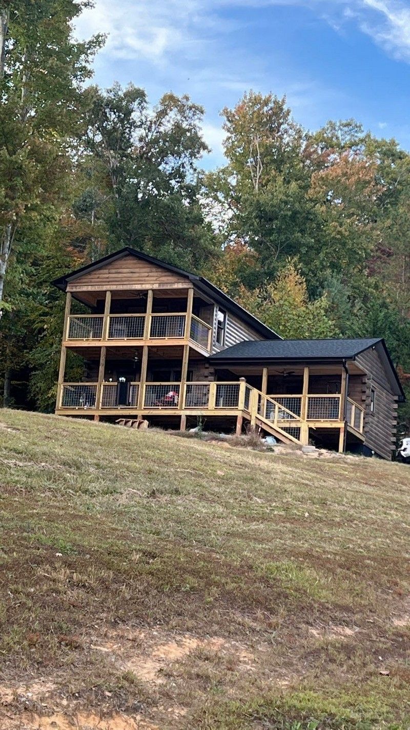 A large wooden house is sitting on top of a grassy hill surrounded by trees.