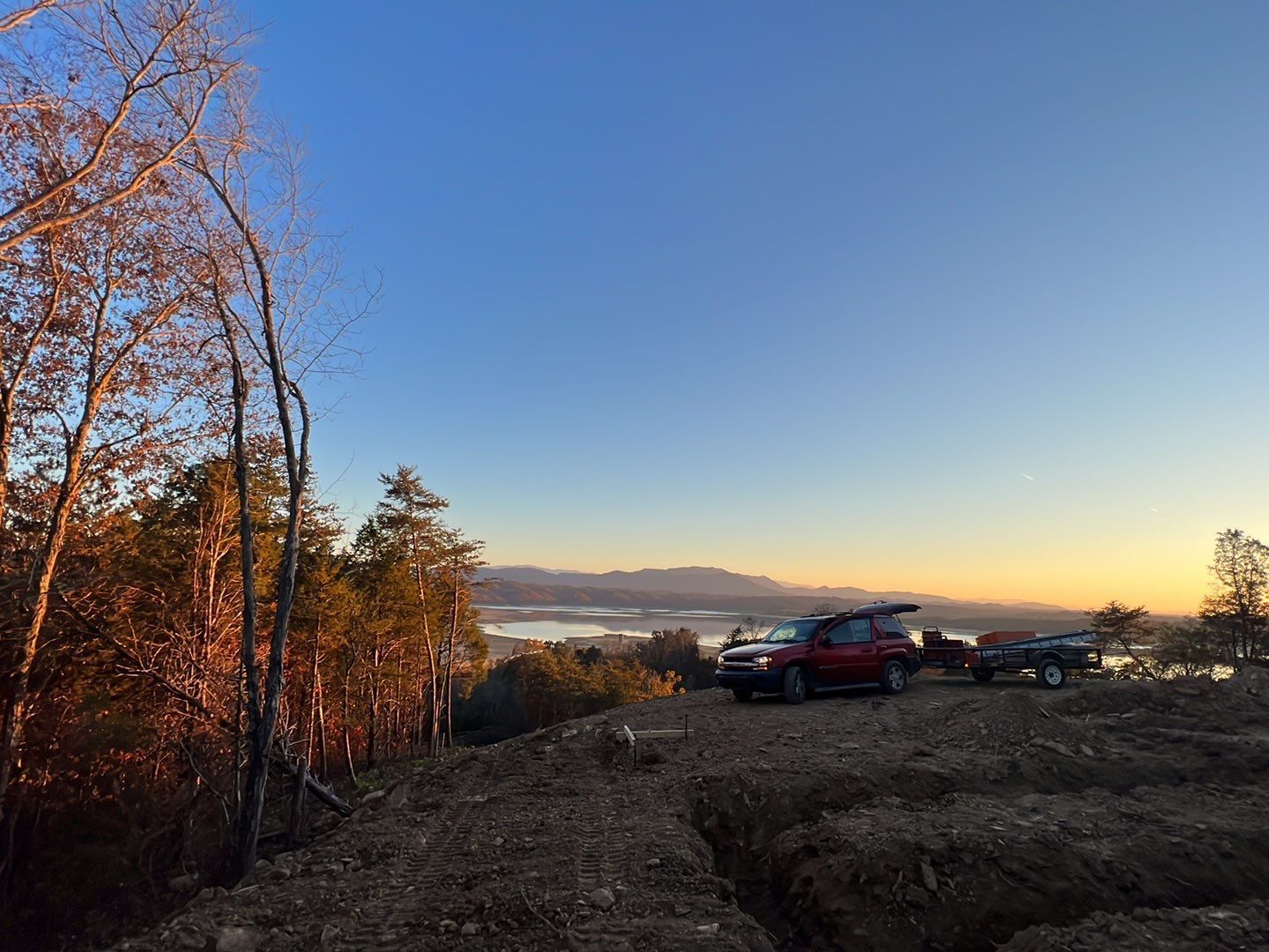 A couple of cars are parked on top of a hill at sunset.