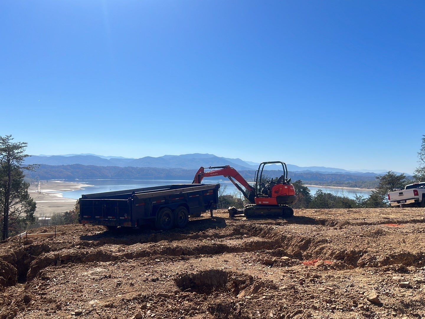 An excavator is digging a hole in a dirt field with mountains in the background.