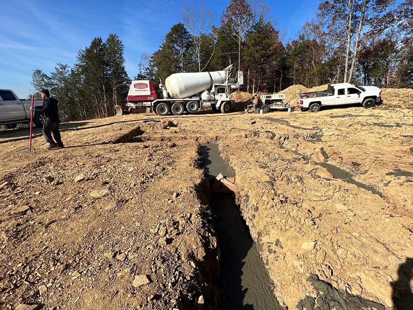 A concrete mixer truck is driving down a dirt road.