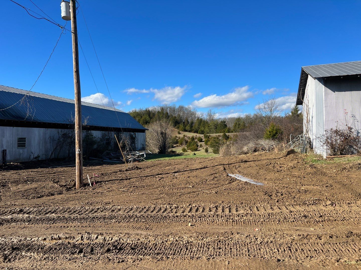 A dirt field with a telephone pole and a barn in the background.