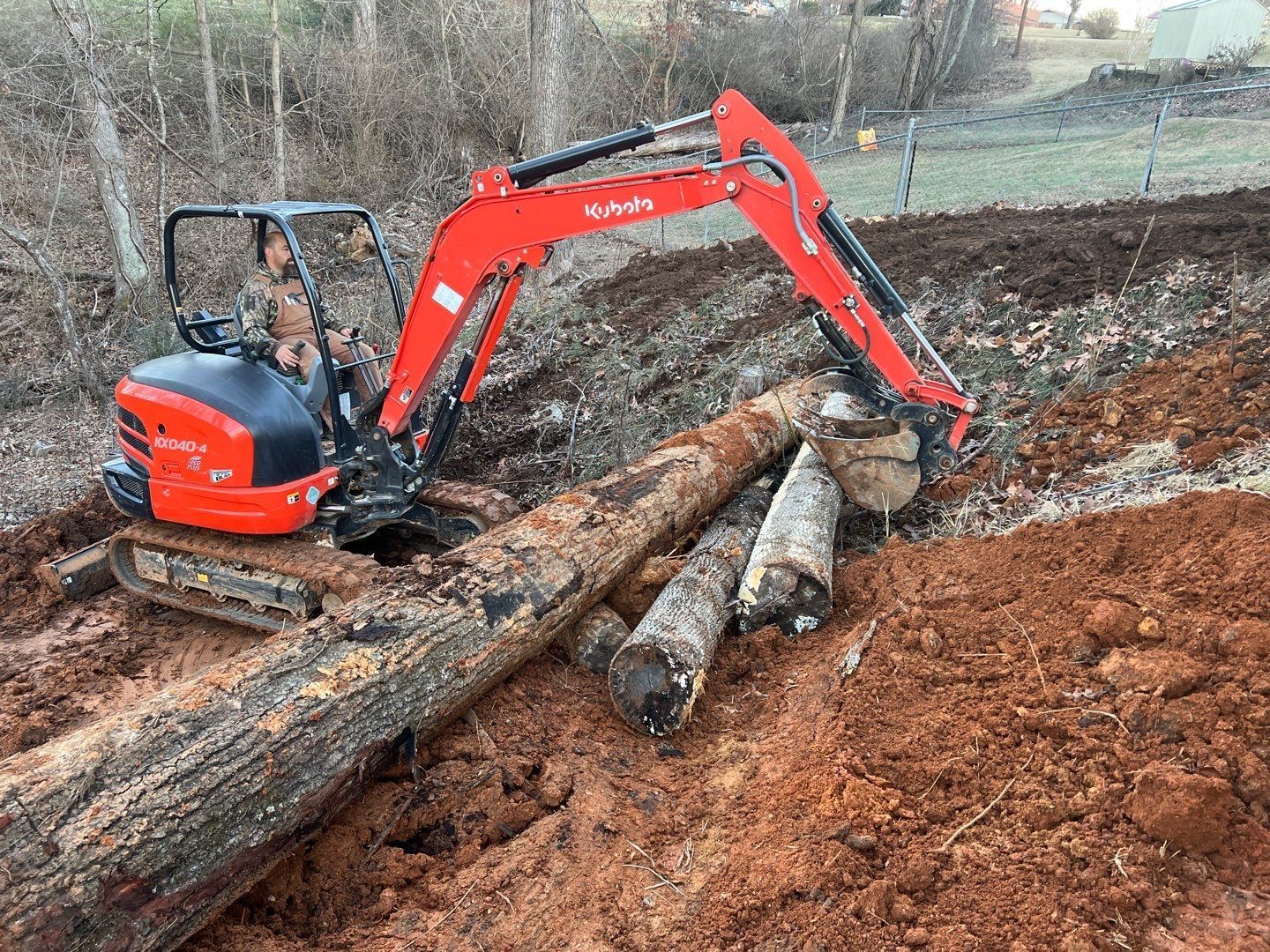 A red and black excavator is digging a hole in the dirt.