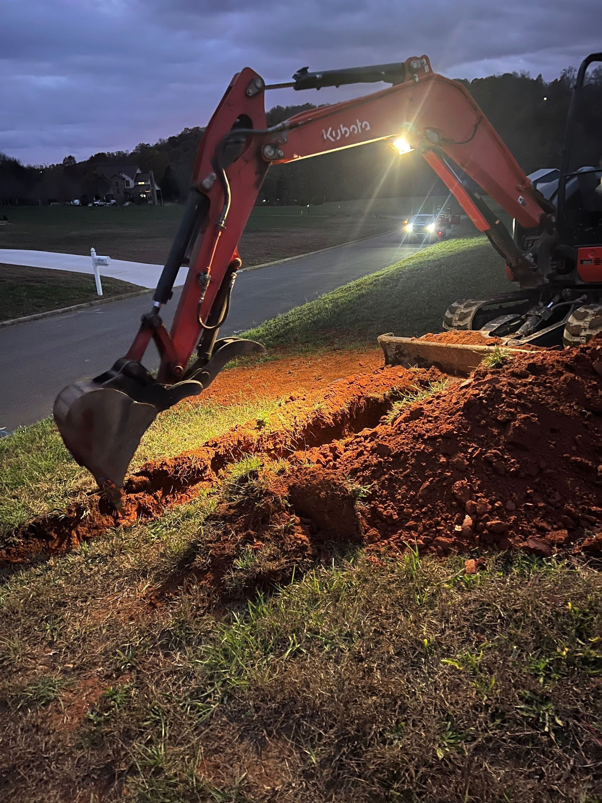 A red excavator is digging a hole in the ground at night.