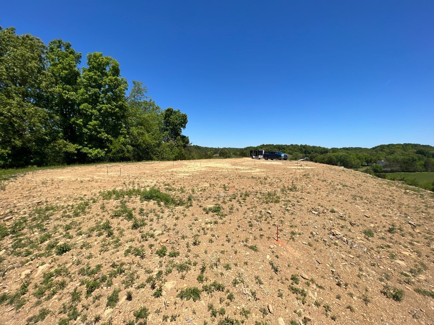 A dirt field with trees in the background and a blue sky