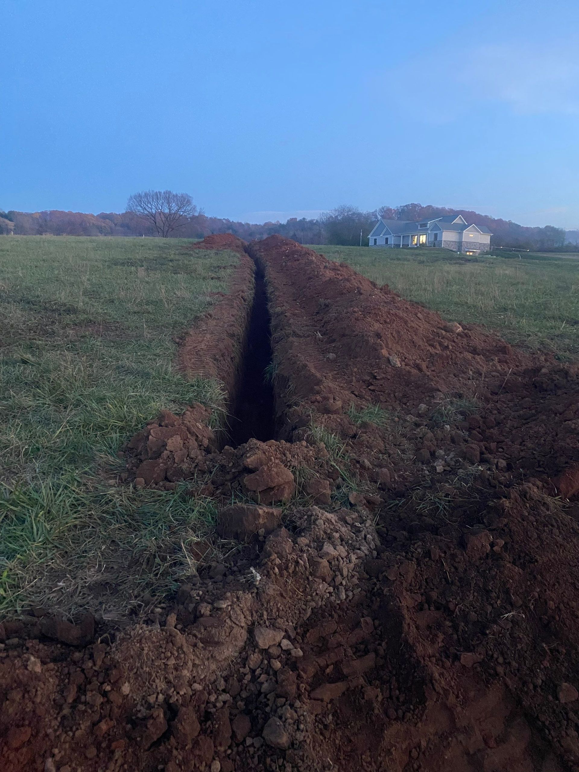 A dirt road going through a grassy field with a house in the background.