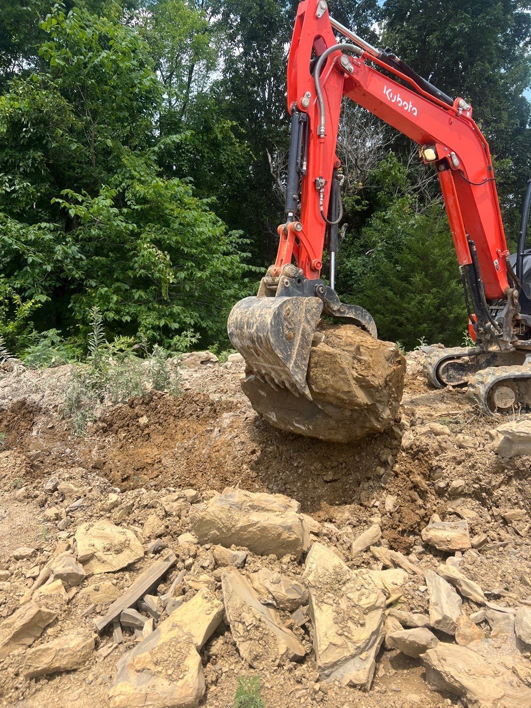 A red excavator is moving a large rock in the dirt.