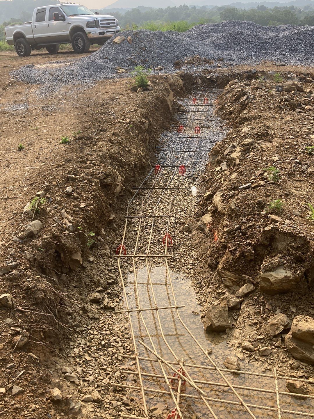 A white truck is parked next to a trench in the dirt.