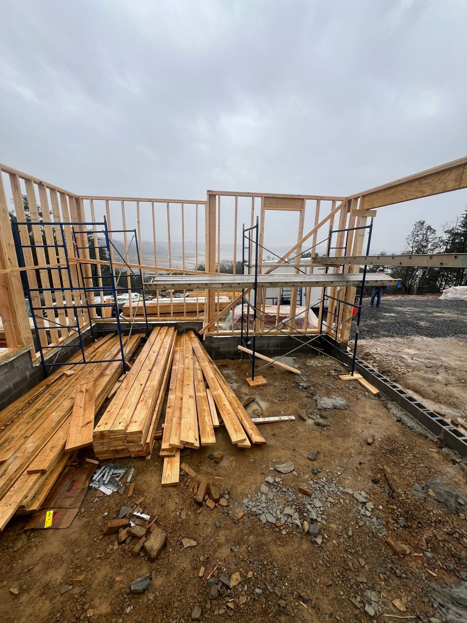 A pile of wood is sitting on the ground in front of a building under construction.