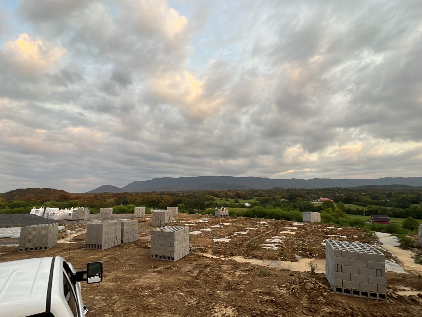 A white truck is parked in a dirt field with a cloudy sky in the background.