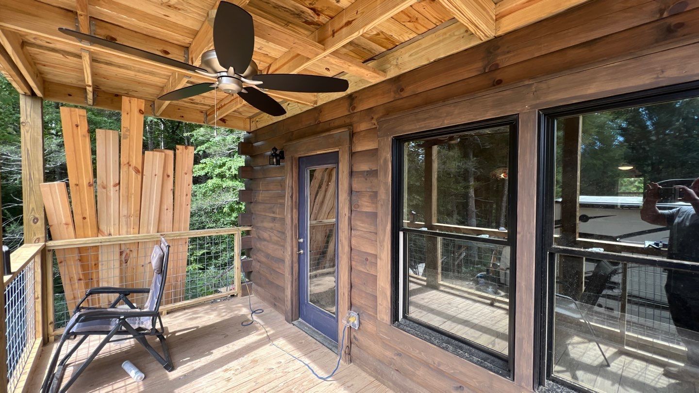 There is a ceiling fan on the porch of a cabin.