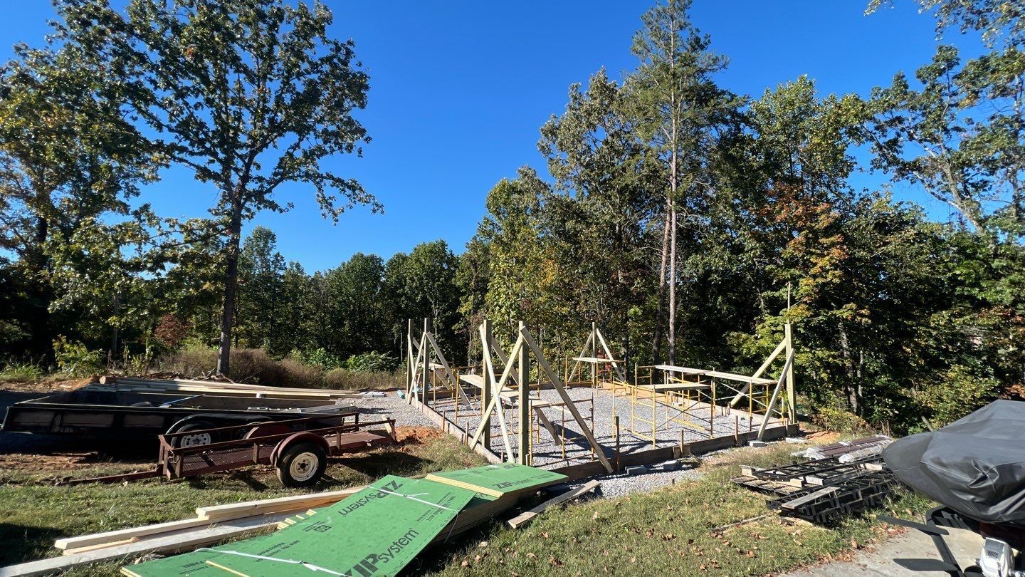 A construction site with a green tarp on the ground and trees in the background.