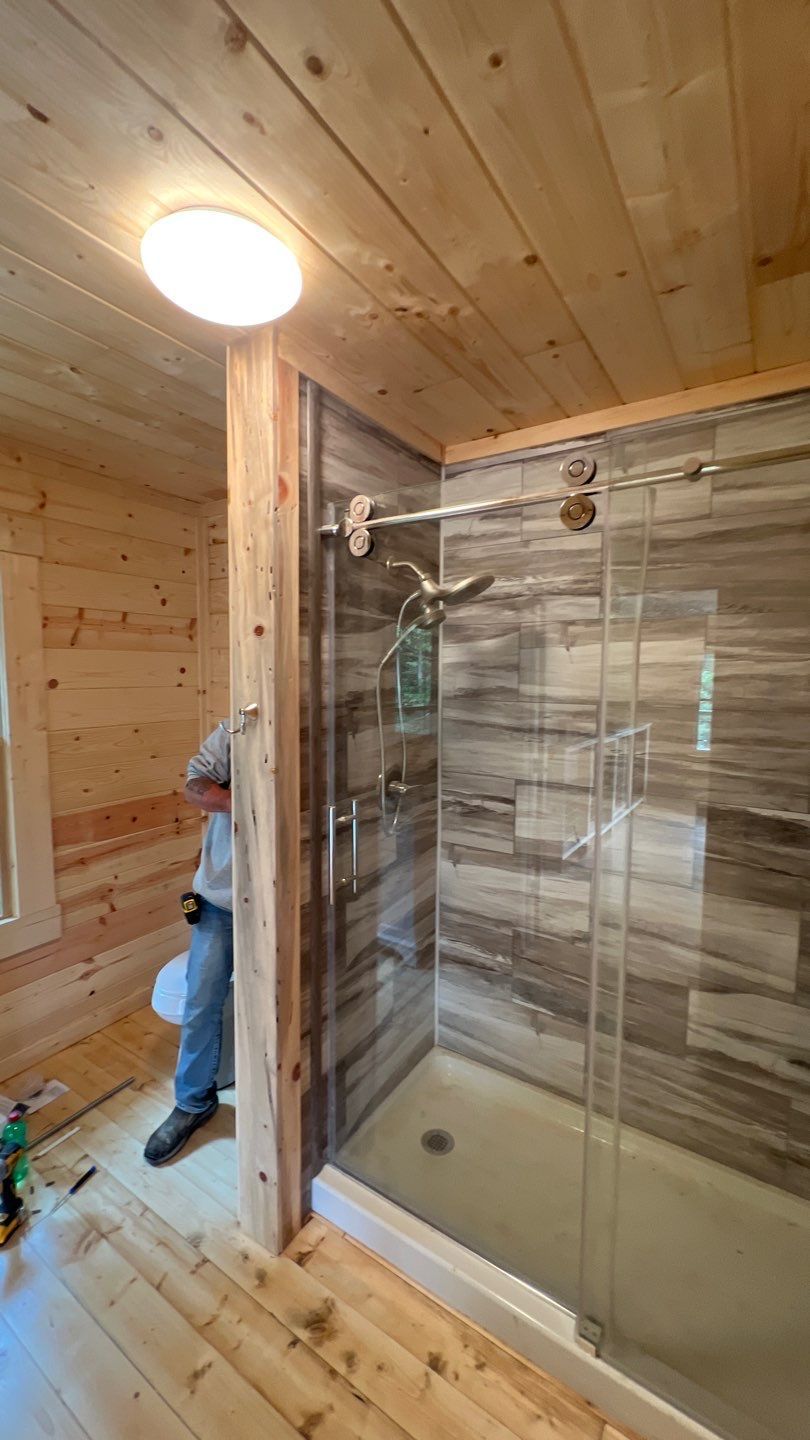 A man is standing in a bathroom with a walk in shower.