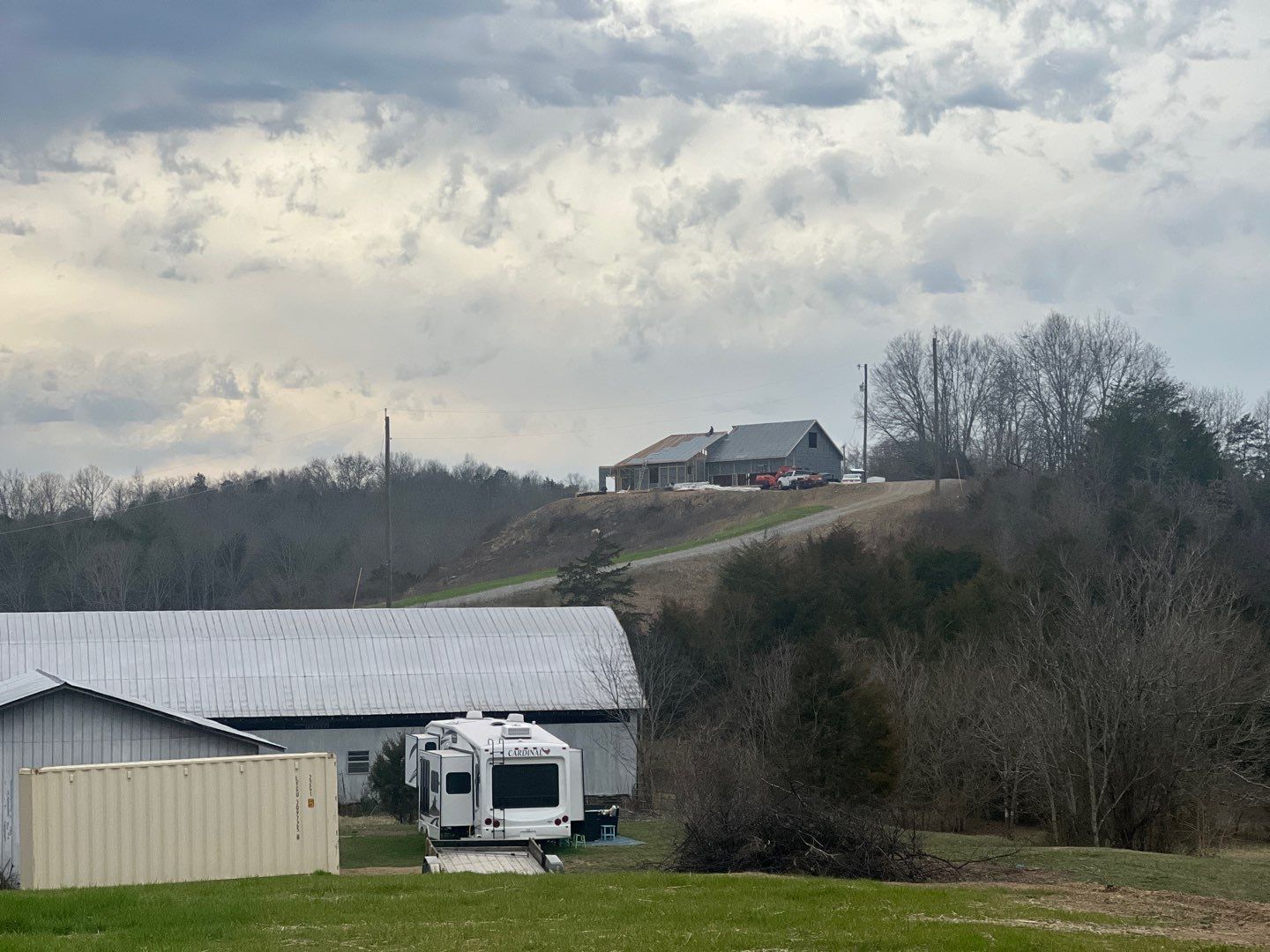 A rv is parked in front of a barn on a hill.