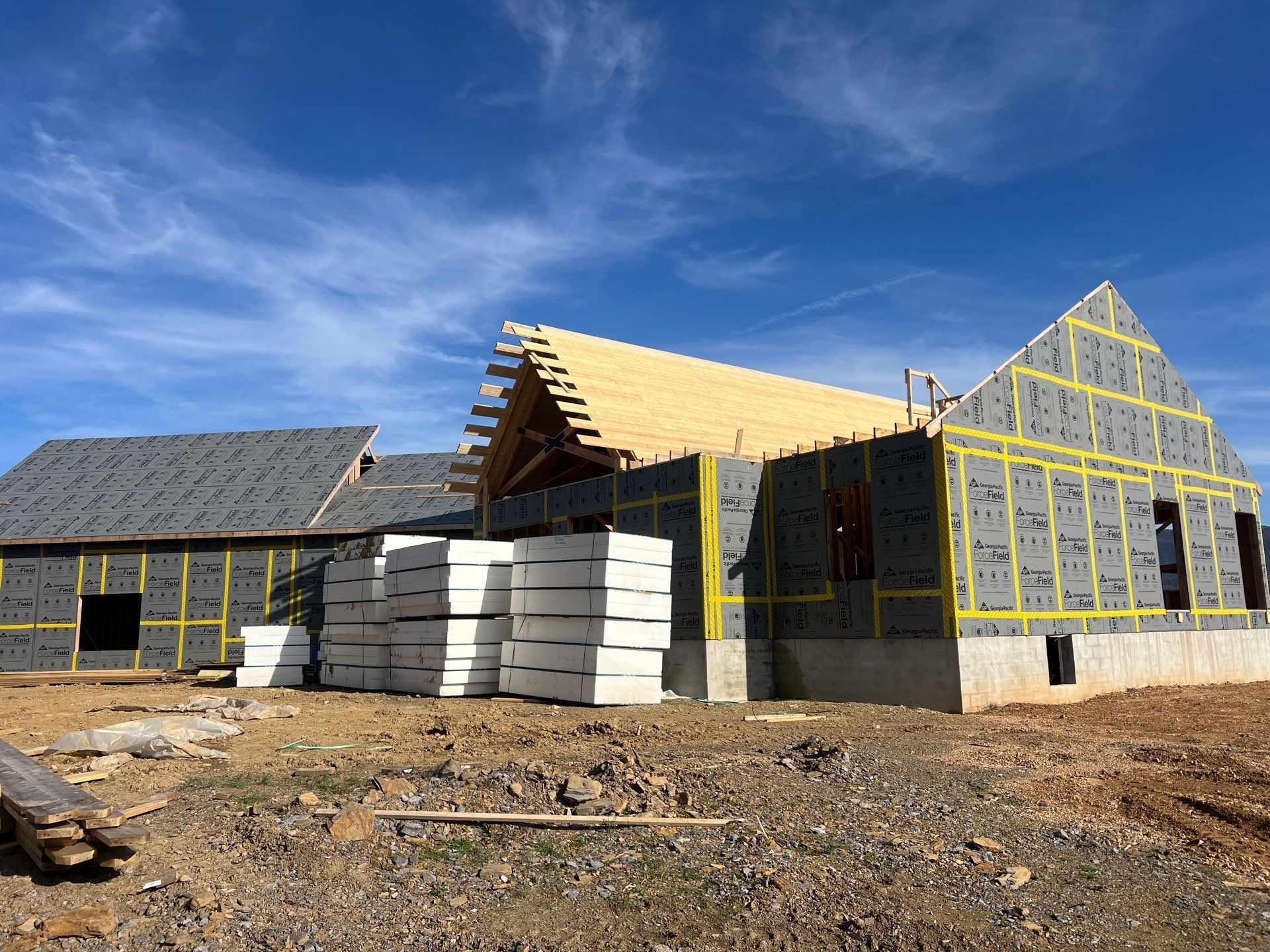 A house is being built in a dirt field with a blue sky in the background.