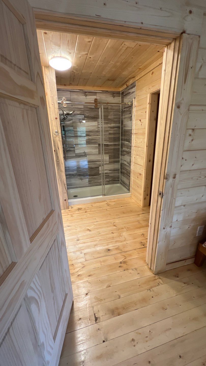 A wooden hallway leading to a bathroom with a walk in shower.