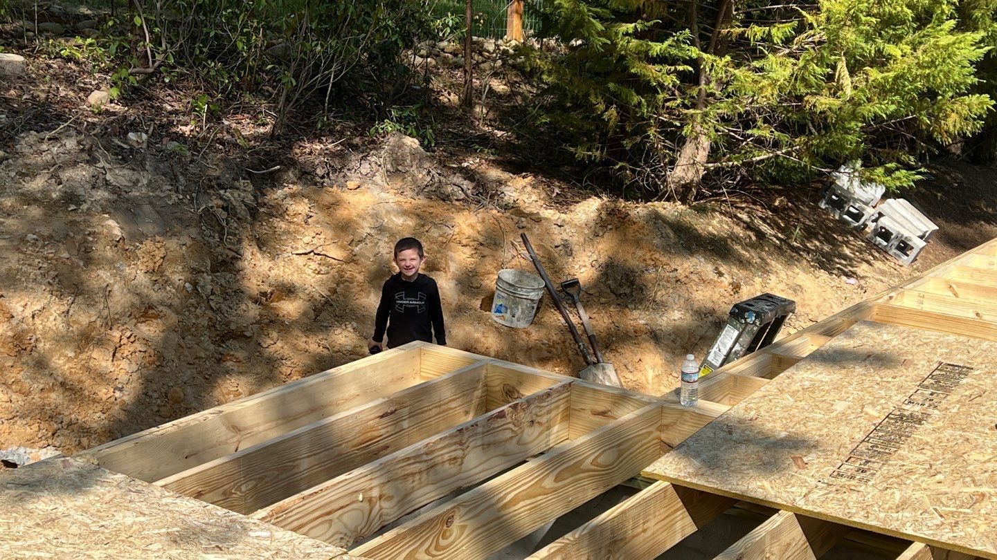 A boy is standing on top of a wooden structure in the woods.