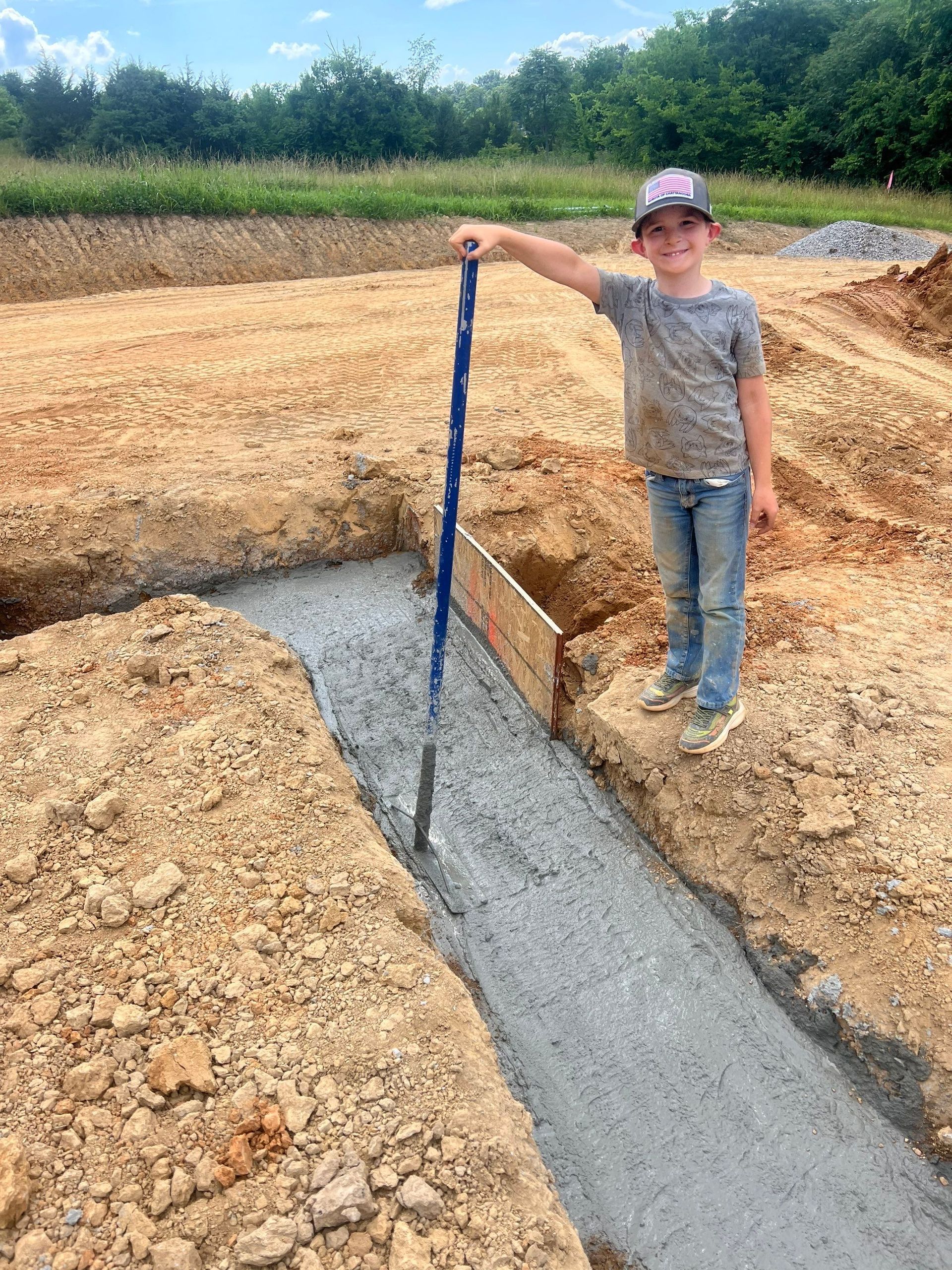 A young boy is standing in the dirt holding a shovel.