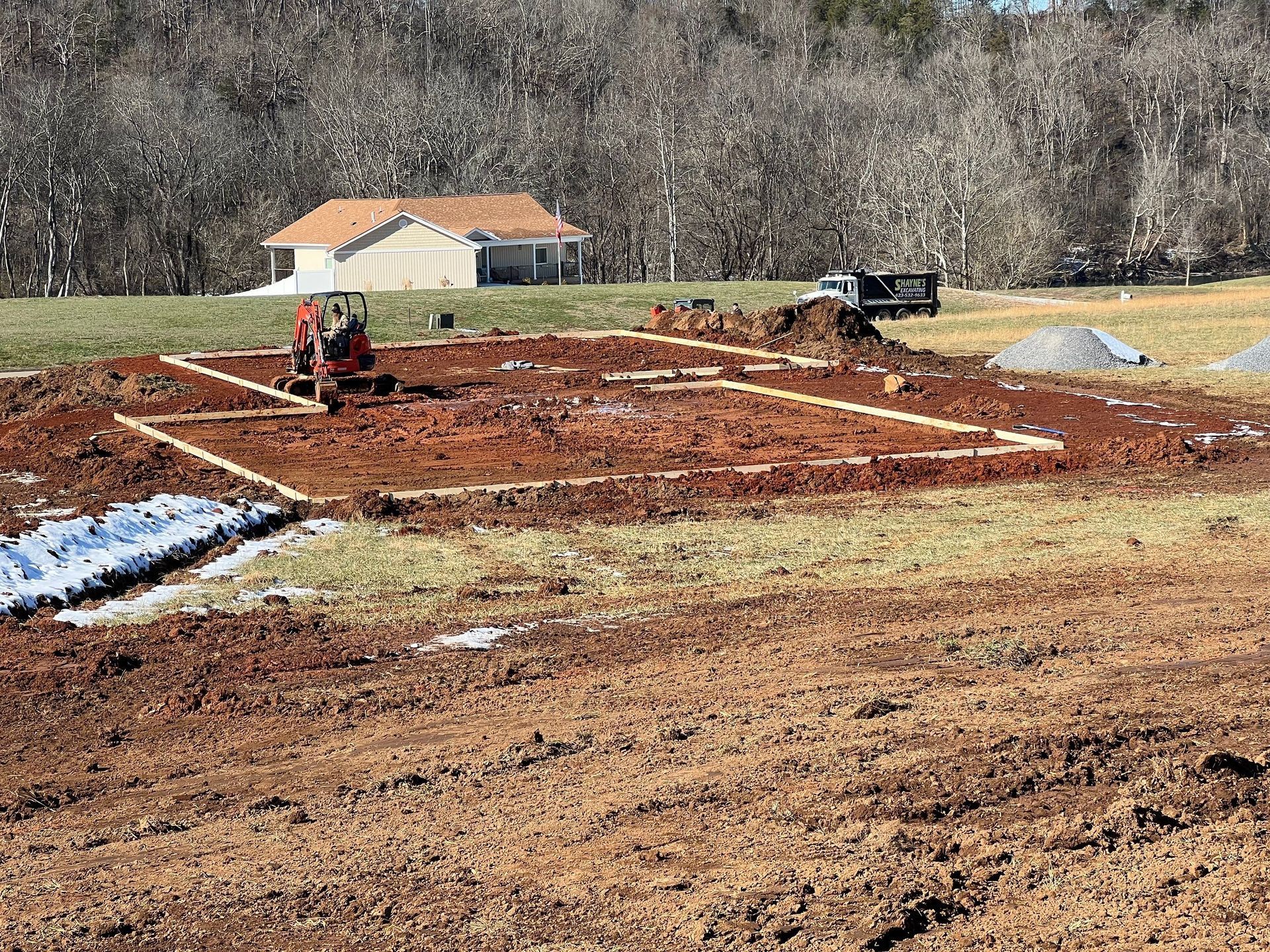 A construction site with a house in the background and a tractor in the foreground.