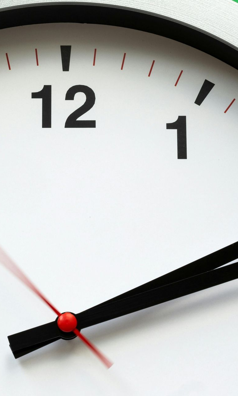 Clock face showing the time slightly past 12:00. Black hands, red second hand. White background.