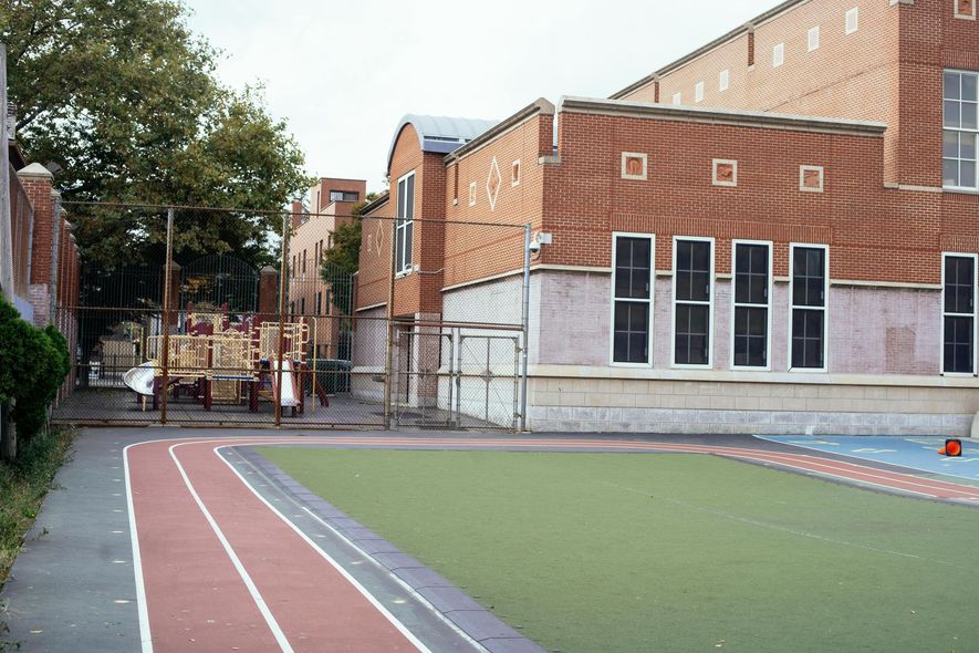 Schoolyard with track, playground, and brick building. Green turf area, red running track.