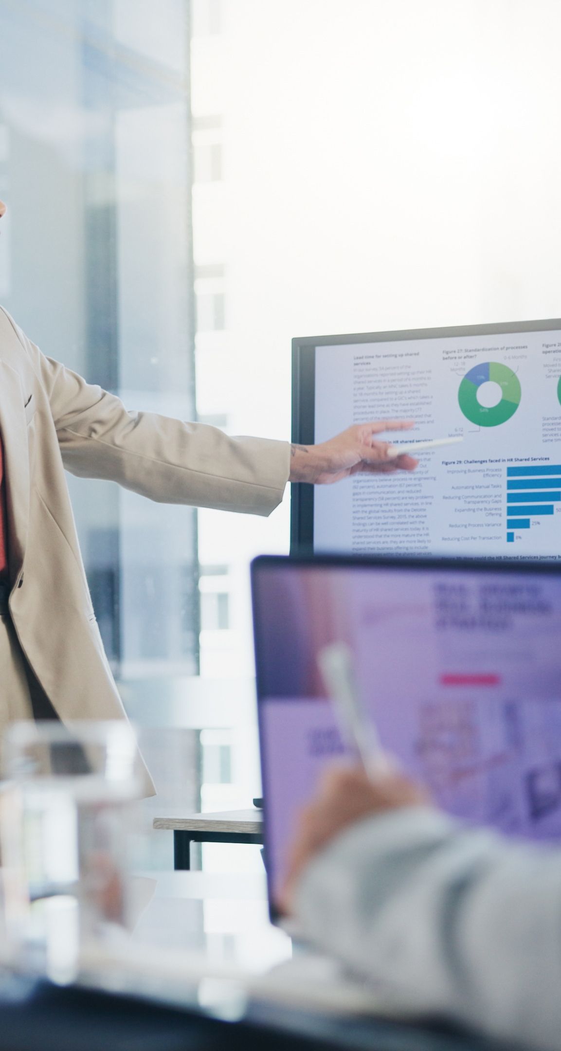 Woman pointing at a bar graph on a monitor during a presentation. Laptop in the foreground.