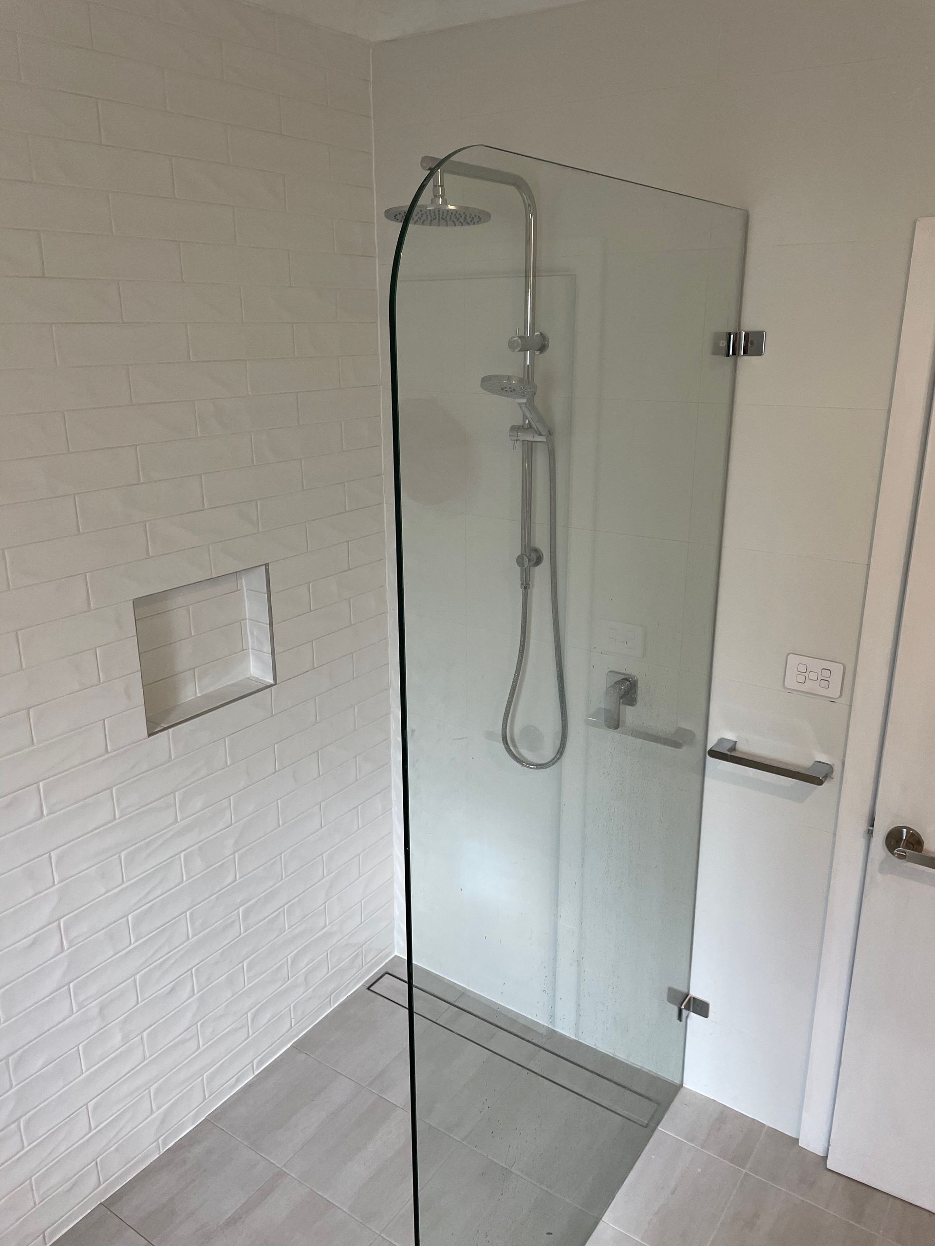 A bathroom with a walk in shower with a glass door and a shower head.