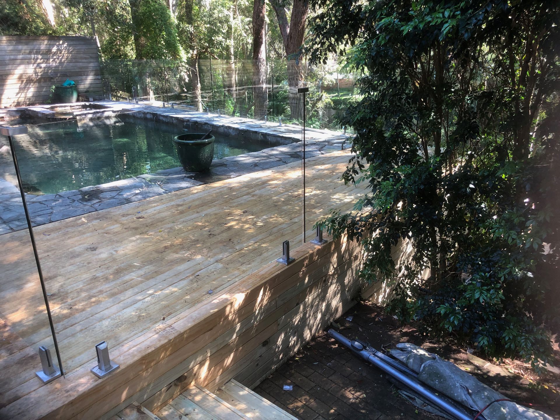 A wooden deck with a glass railing overlooking a swimming pool.