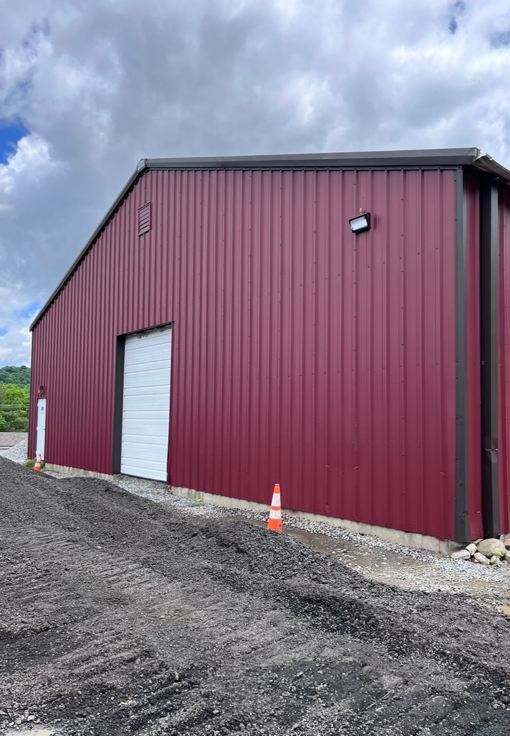 A red metal building with a white garage door is sitting on top of a dirt road.