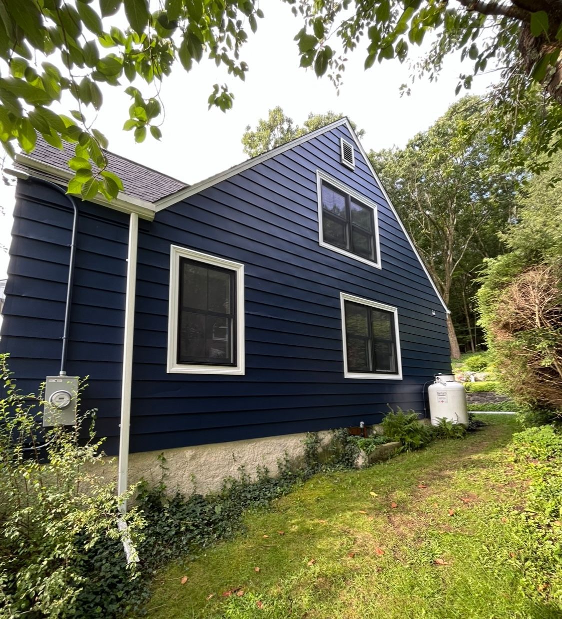 A blue house with white trim and windows is surrounded by trees and grass.