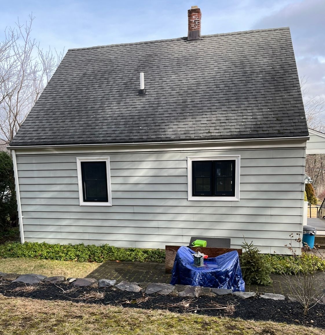 A small white house with a black roof and a blue table in front of it.