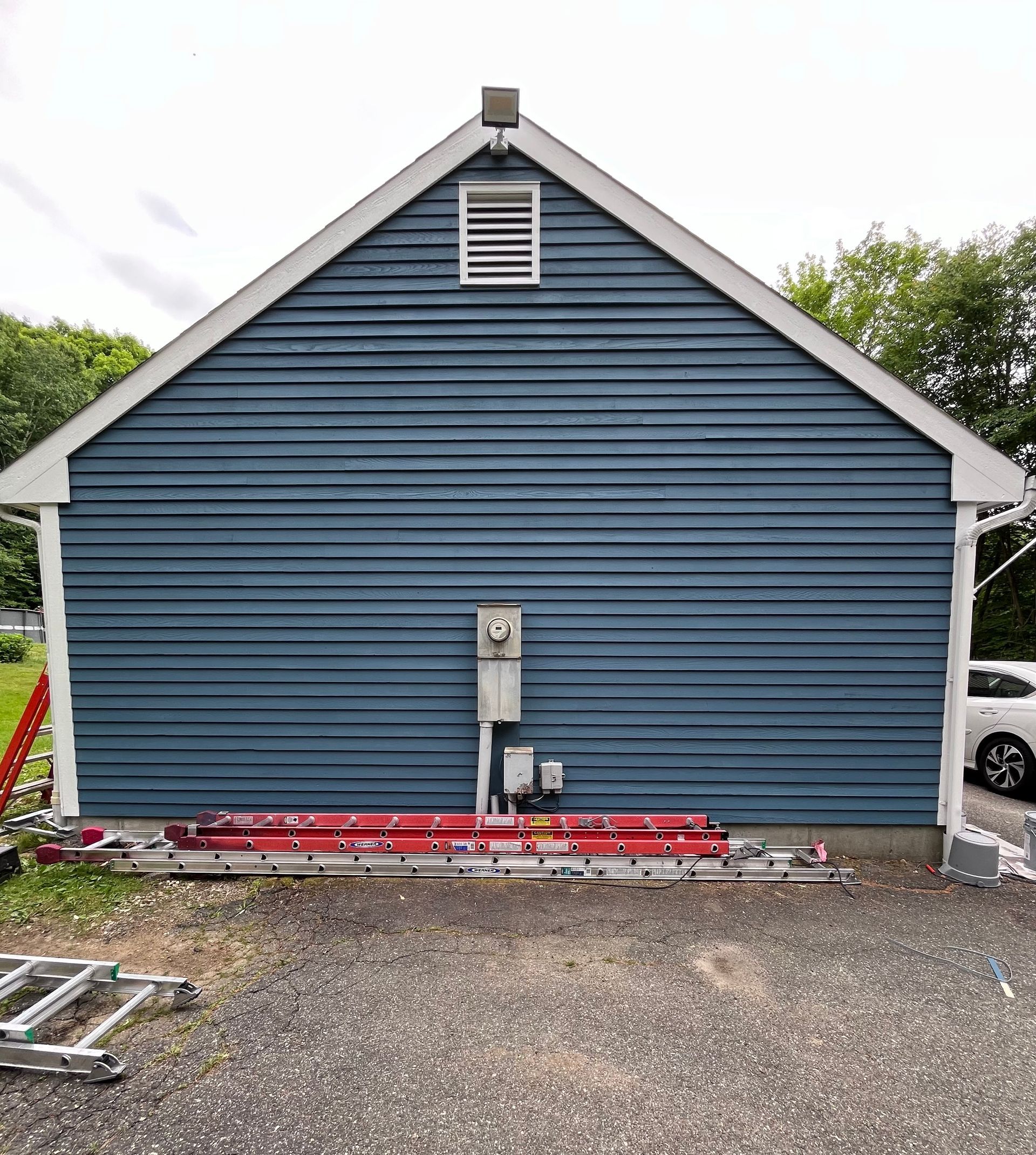 A blue house with a white roof and a ladder in front of it.